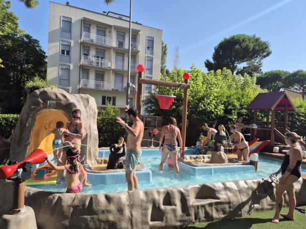 Famiglie giocano in piscina all'aperto con giochi d'acqua.