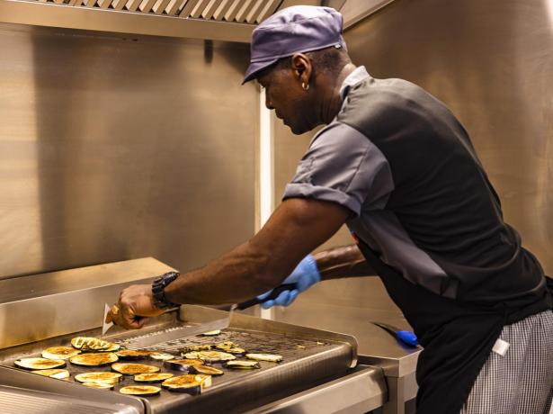 Chef grills vegetables on a griddle in a professional kitchen.