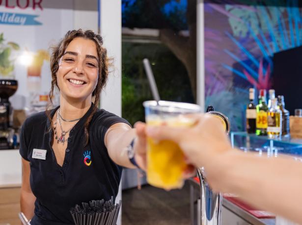 Barista sorridente porge una bevanda fresca in un locale accogliente.