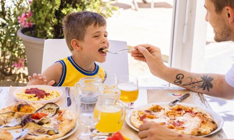 Padre e figlio mangiano pizza e frutta all'aperto.