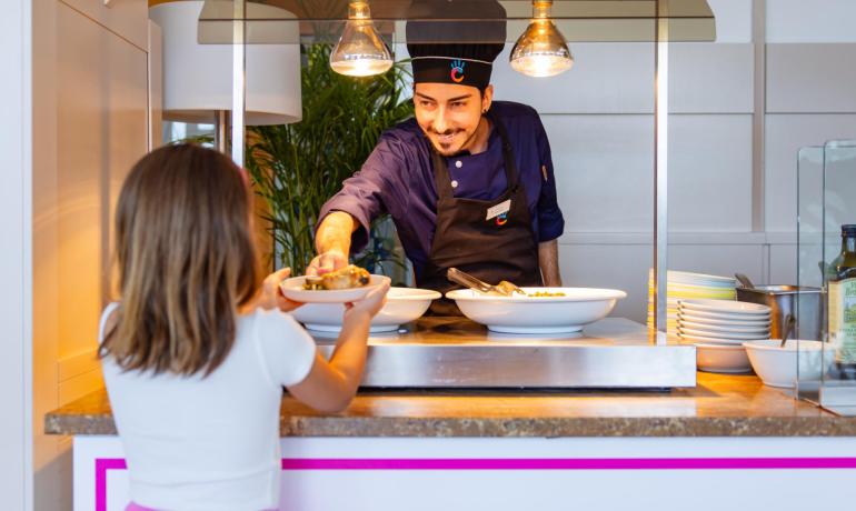 Cuoco serve cibo a bambina in mensa luminosa.