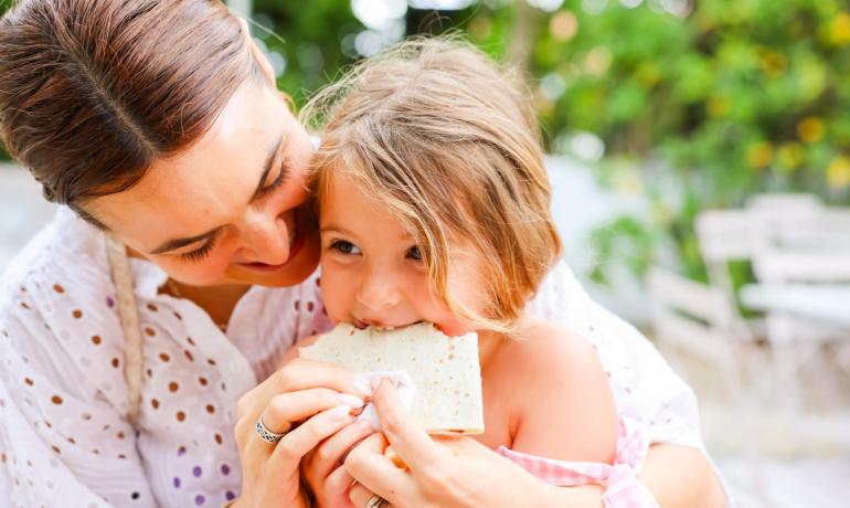 Mère et fille partagent un repas en plein air, souriant joyeusement.