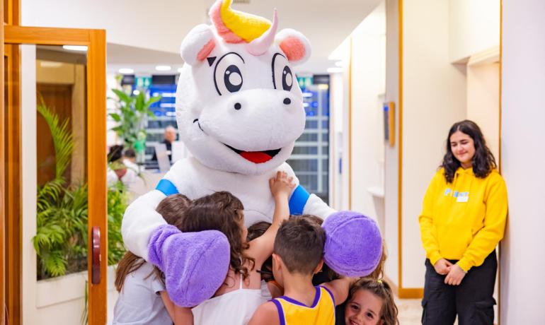 Children hug a unicorn costume in a joyful setting.