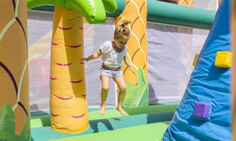 Child jumping on a colorful inflatable castle with palm trees.