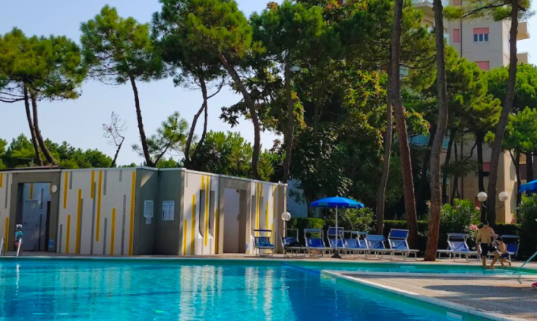 Piscina all'aperto con lettini e ombrelloni, circondata da alberi.