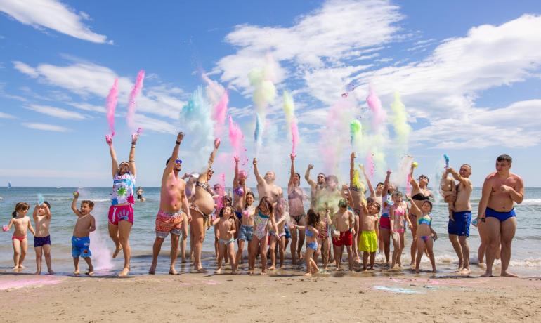 Gruppe von Menschen wirft bunte Pulver am Strand.