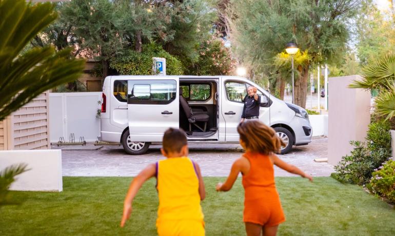 Bambini corrono verso un furgone con un uomo che saluta.