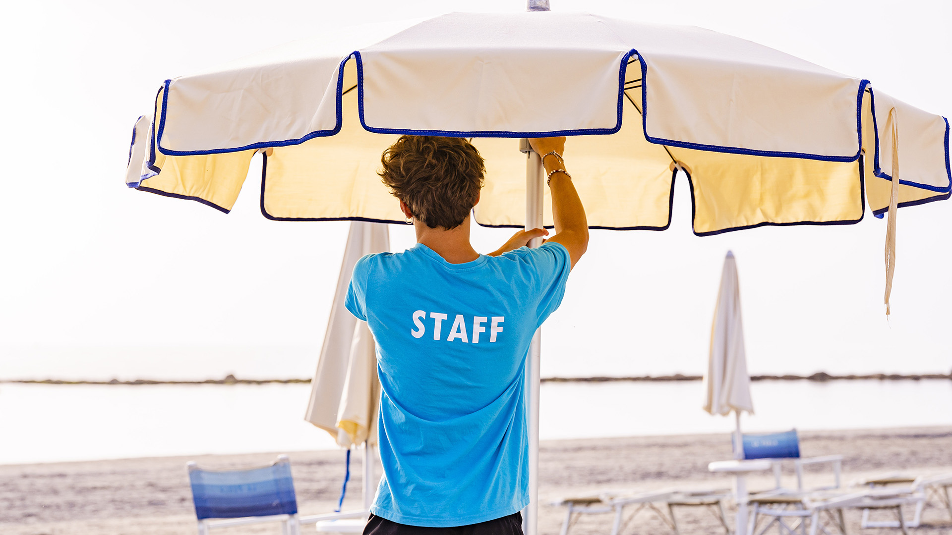 Famiglia cammina sulla spiaggia, tra ombrelloni e sdraio, verso il mare.