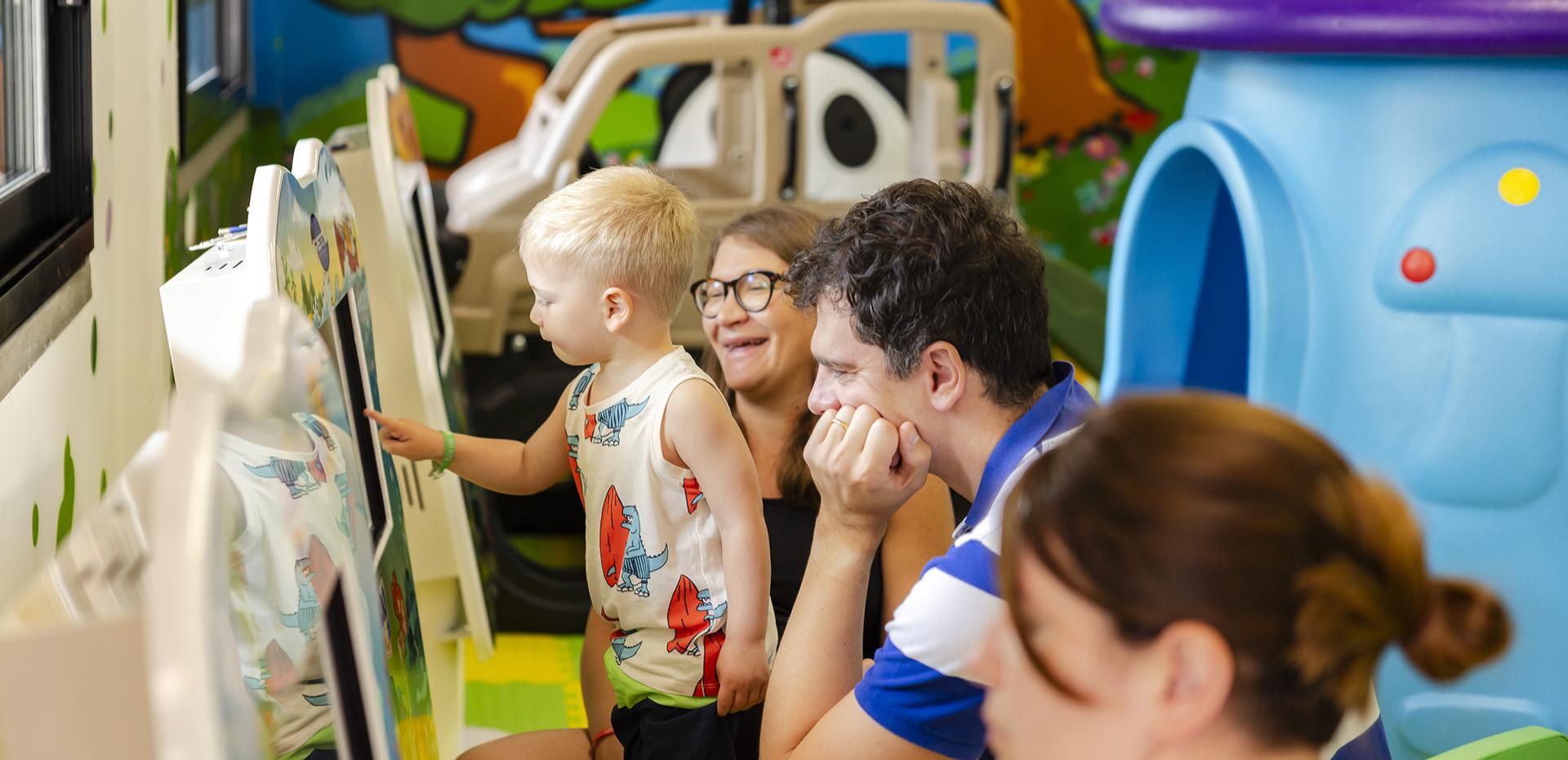 Child plays joyfully in a colorful play area with family.