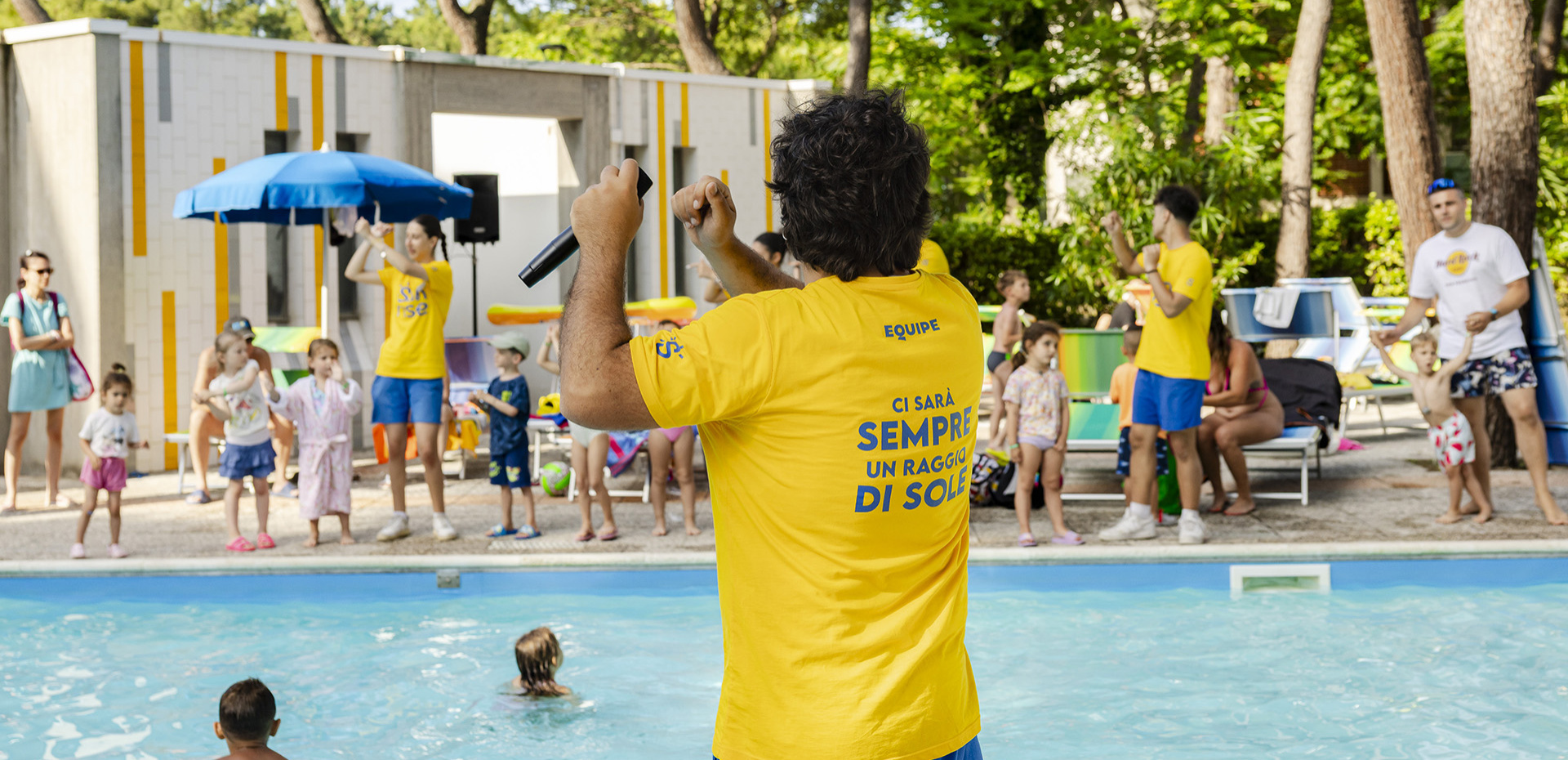 Bambini giocano a basket sulla spiaggia, guidati da un'istruttrice in maglietta rossa.