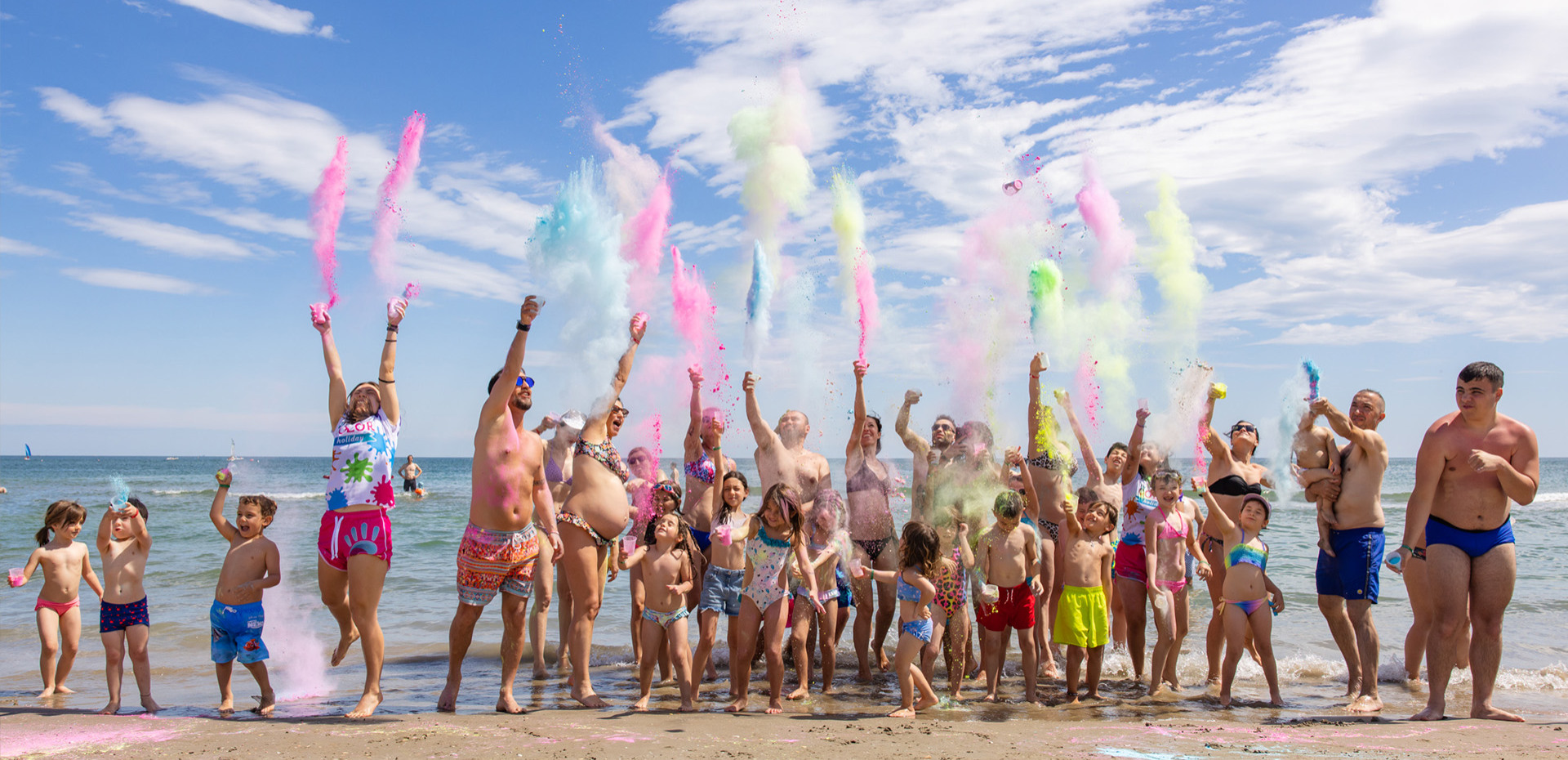 Bambini e adulti sorridenti al mare con bicchieri di plastica colorati.