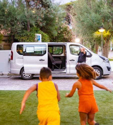 Children joyfully run towards a van with a smiling person.