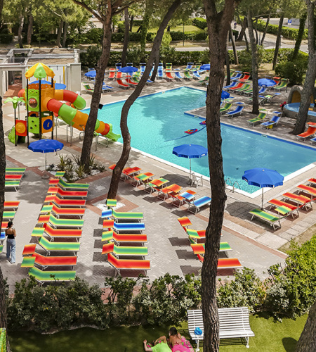 Colorful, lively pool area with trees, sunbeds, and children's playground.