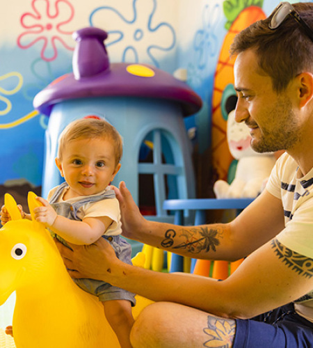 Area giochi per bambini con scivolo giallo e sedie colorate.