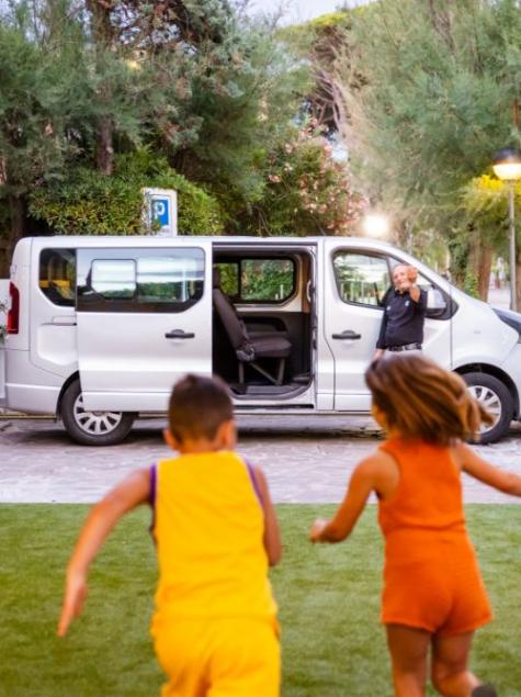 Children joyfully run towards a van with a smiling person.