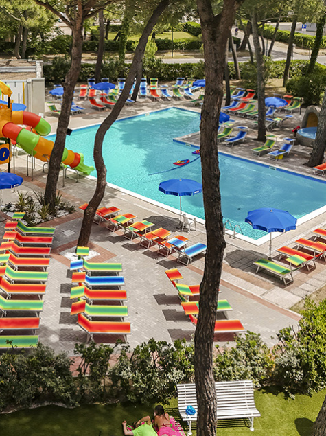 Colorful, lively pool area with trees, sunbeds, and children's playground.