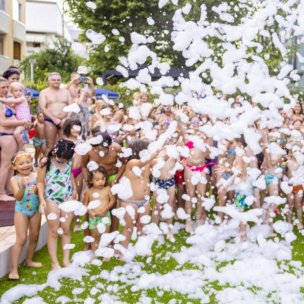 Bambino in culla con lenzuola azzurre, sorridente e vestito di bianco.
