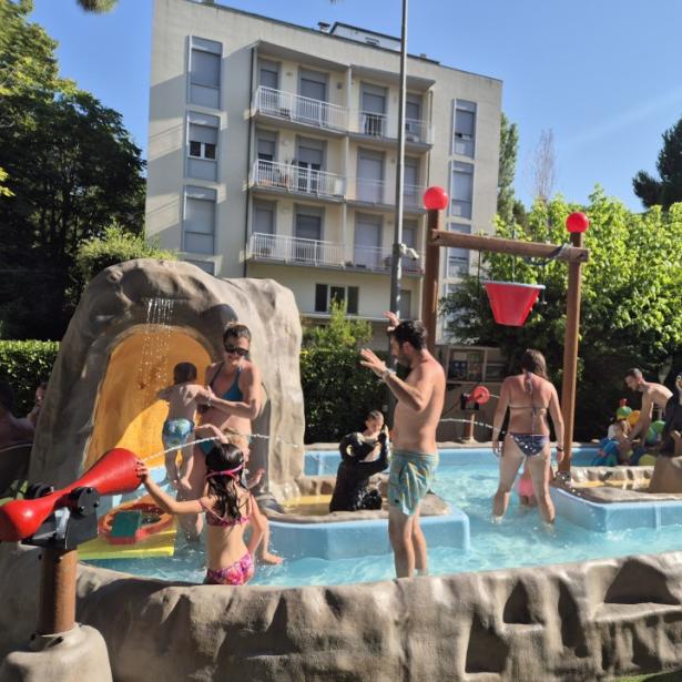 Persone si divertono in una piscina per bambini all'aperto con giochi d'acqua.