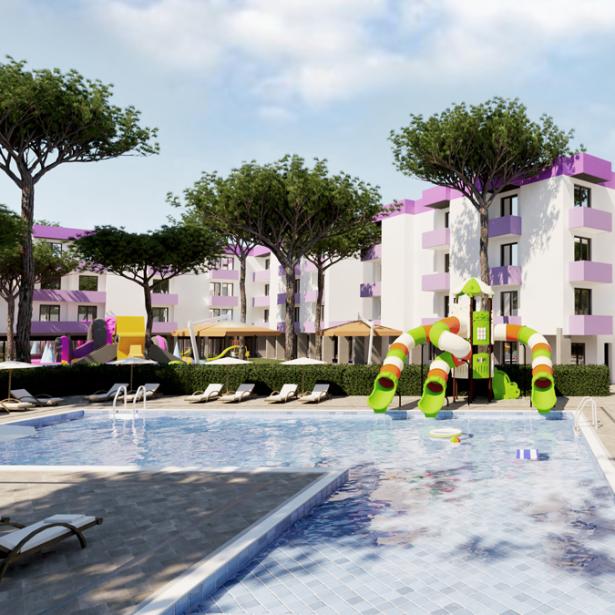 Piscina con scivoli colorati, lettini e palazzi con dettagli viola, circondati da alberi.