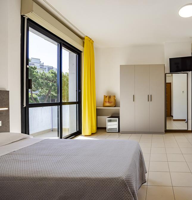 Chambre lumineuse avec rideaux jaunes et deux lits, ambiance chaleureuse.