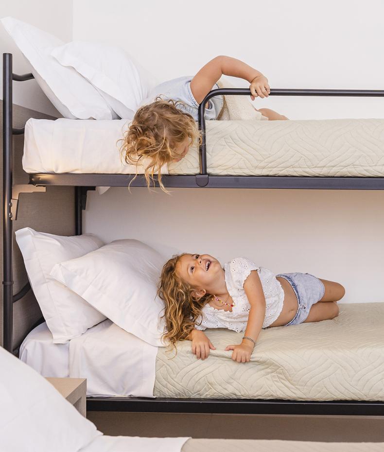 Bambina salta sul letto, mentre una donna incinta la osserva sorridendo.